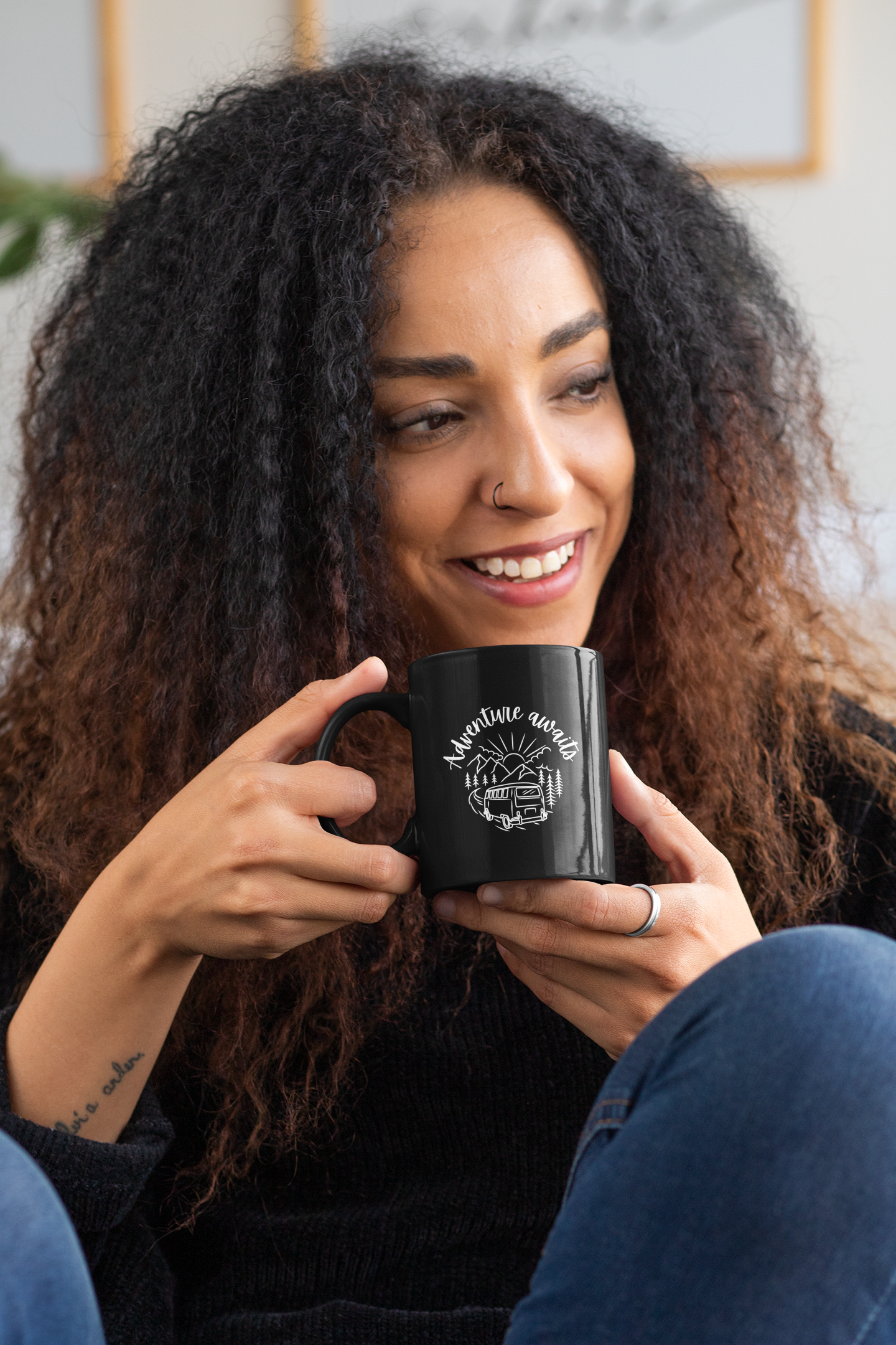Smiling curly-haired woman holding a black ceramic coffee mug.
