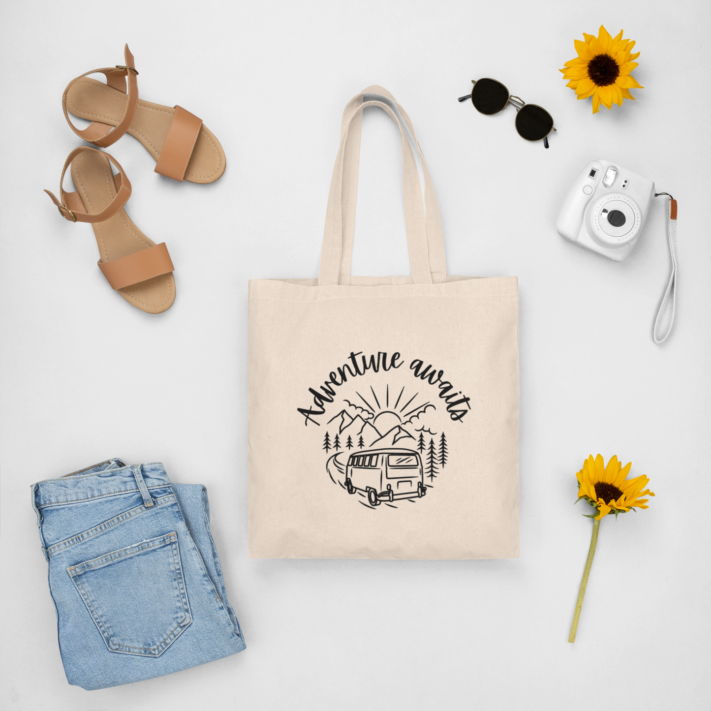 Canvas tote bag with print "adventure awaits" surrounded by girly spring outfit.