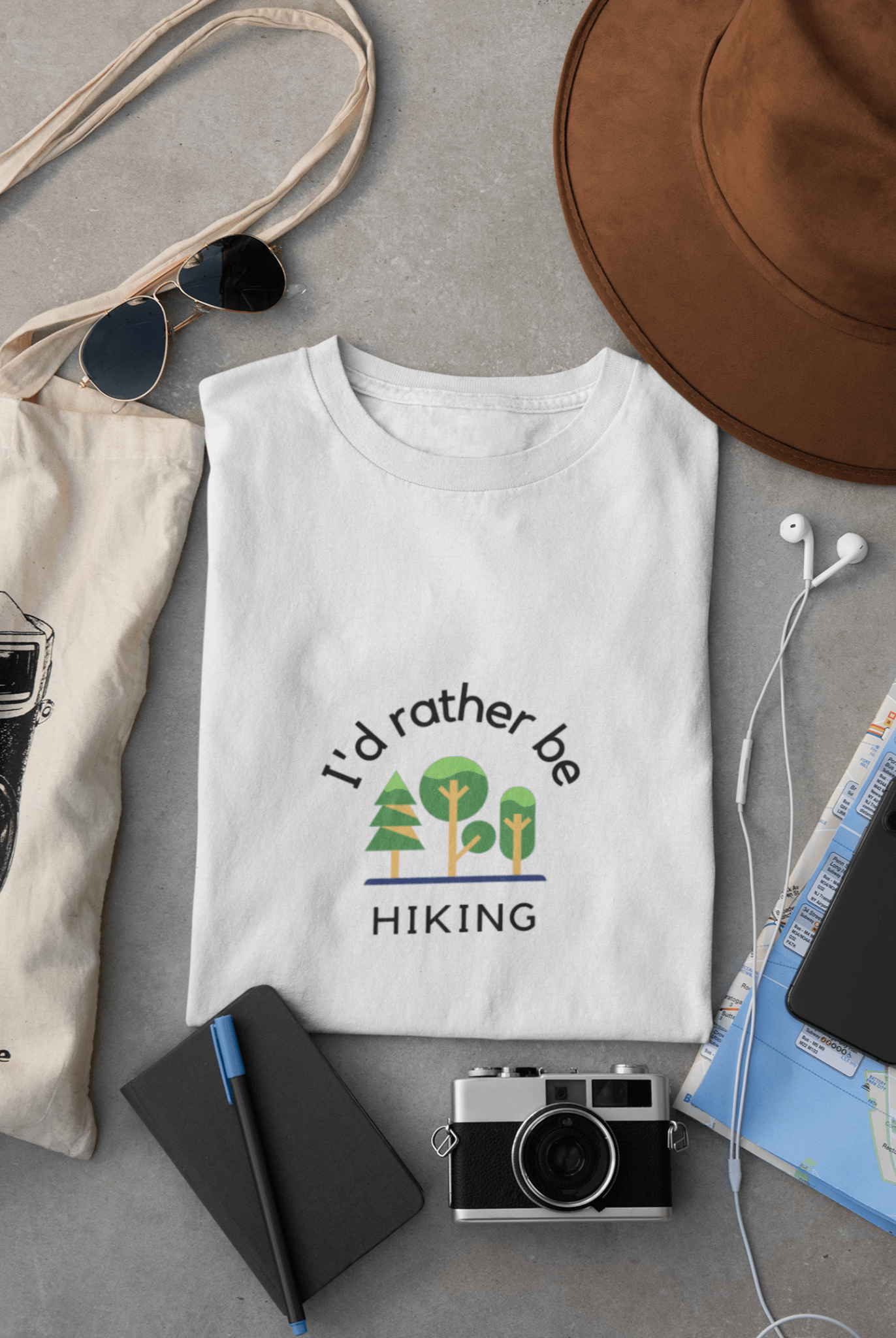Folder white T-shirts with print "I'd rather be hiking" placed between travel accessories.